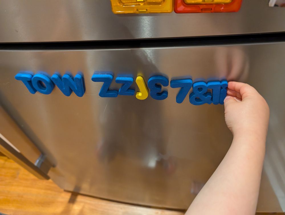 A small child's hand is shown putting magnets on a fridge in random order: TOWZJ37&1i