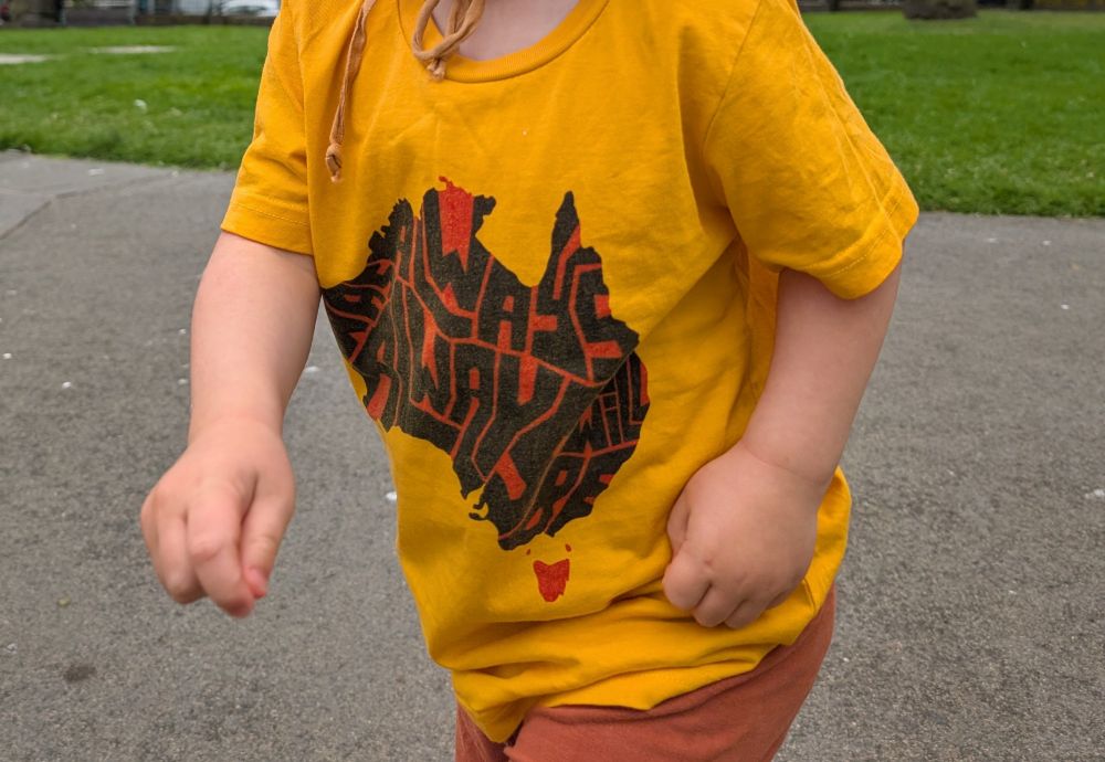 A child wears a yellow t shirt with "always was always will be" on the front