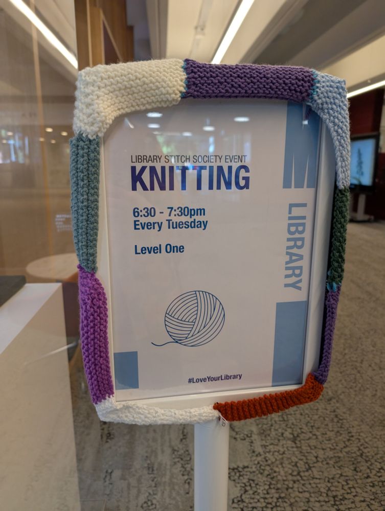 A sign that reads "library stitch society event: knitting", with a knitted wool border