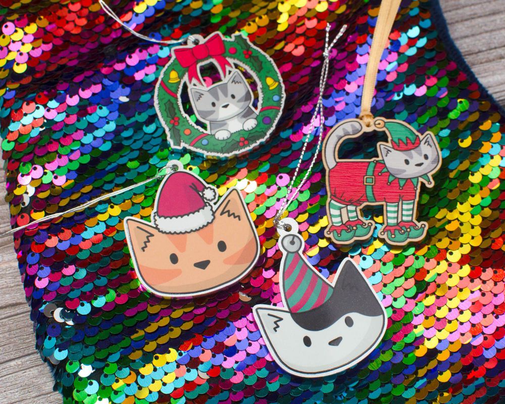four cartoon christmas cat decorations laid out on a rainbow sequin background