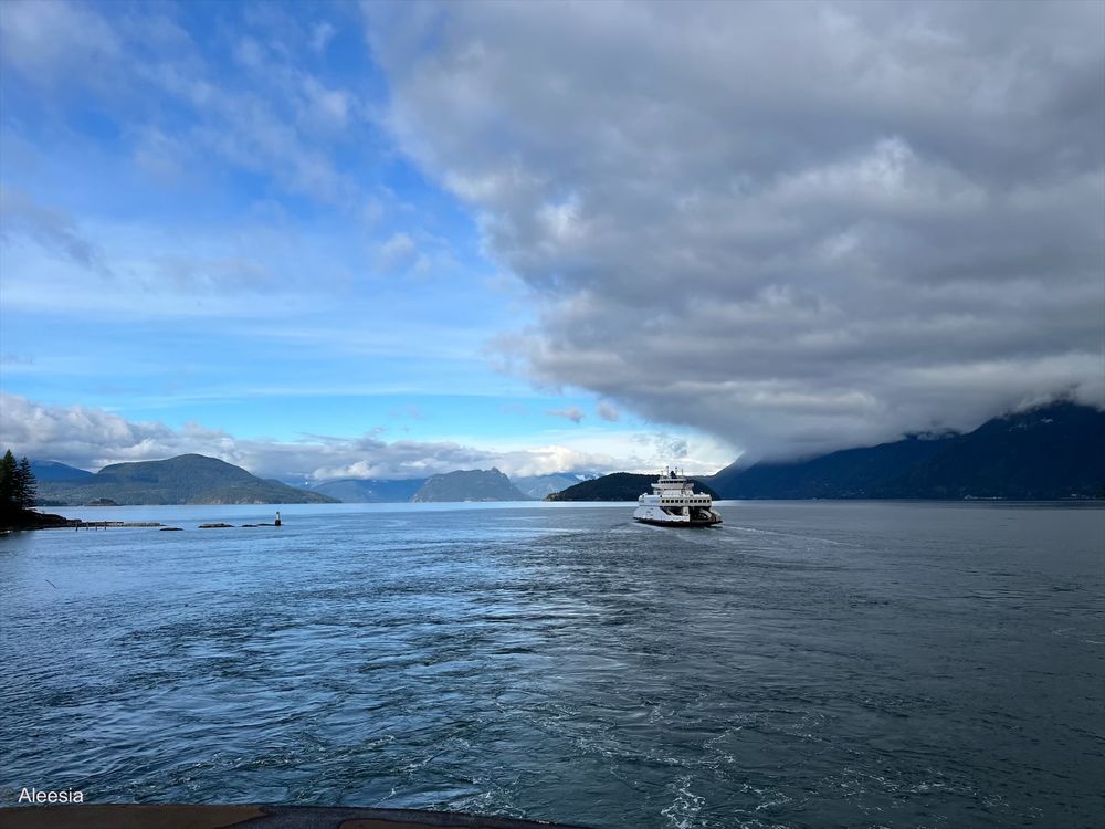 The ferry ride between Vancouver and Nanaimo, British Columbia. The sky is blue with a large cloud hovering above. There are several mountains islands and clouds in the distance.
