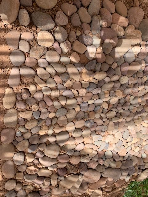 Pebbled footpath with stripes of shade from the bamboo roof screen over a Moroccan house-compound garden.
