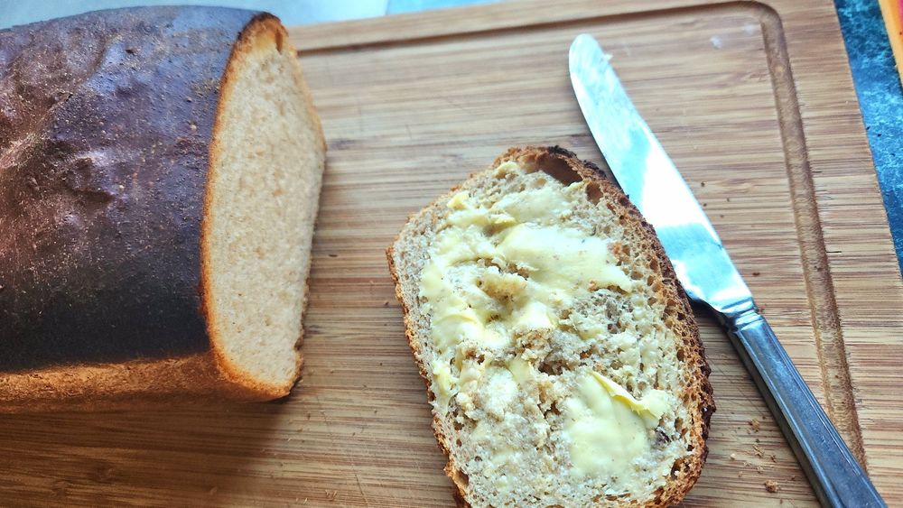 Homemade bread loaf with buttered slice alongside 