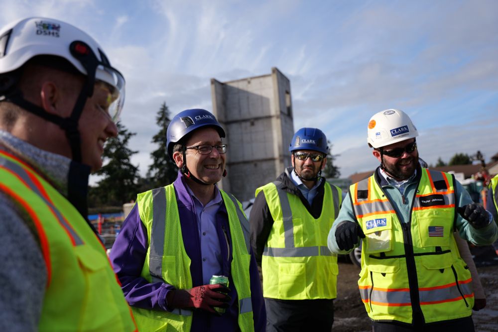 Bob standing in yellow vest and helmet, lime La Croix in hand, with several others and construction in background.
