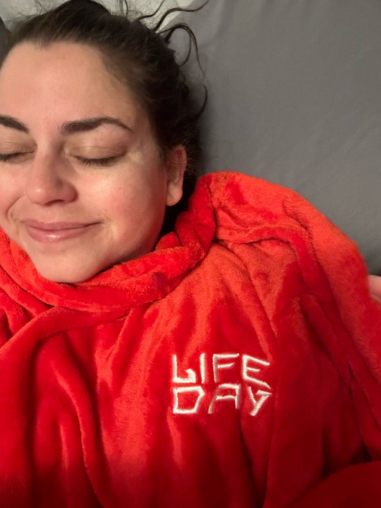 kit laying down in bed with her eyes closed and wearing the fuzzy red Life Day robe