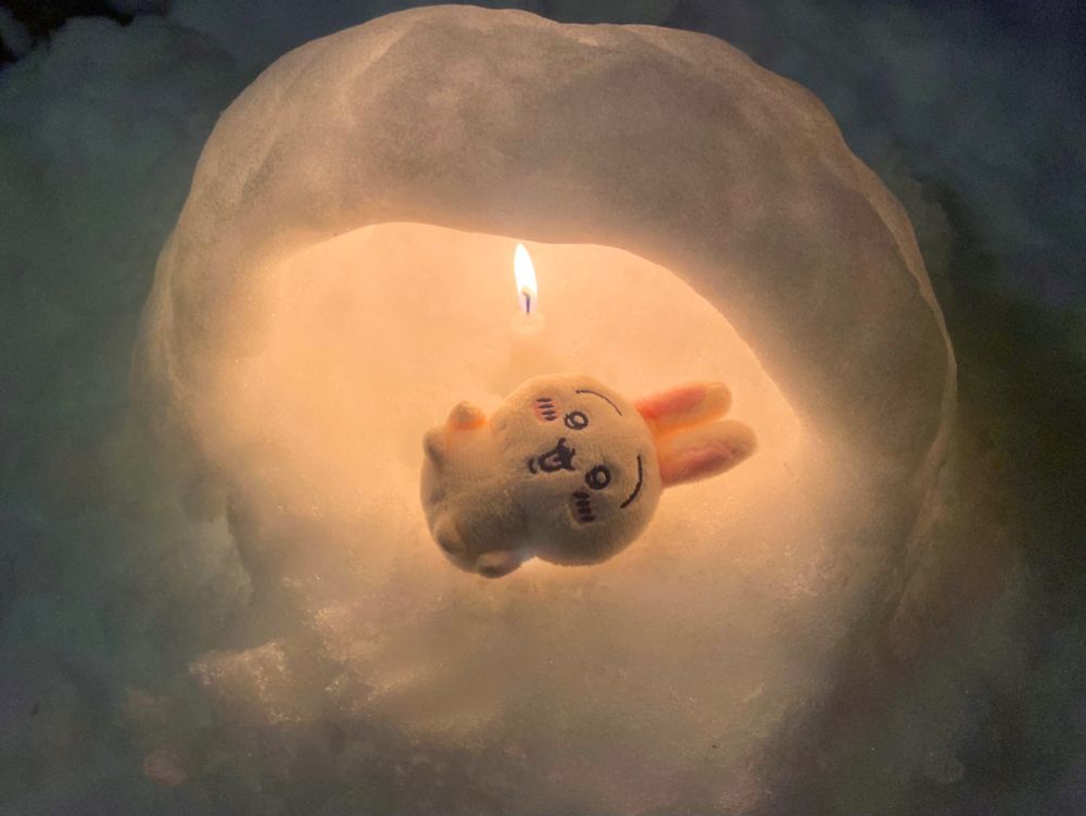 小さな雪のかまくらに灯された火で暖をとるうさぎ