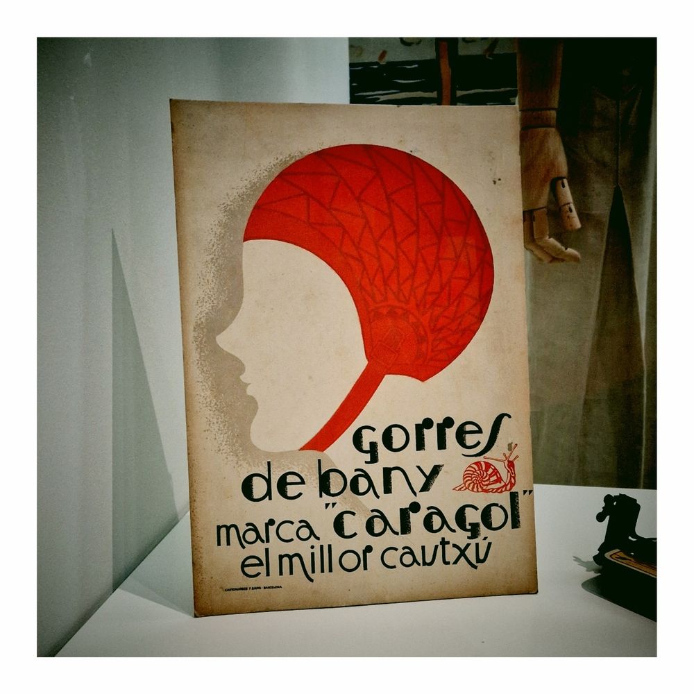 Cartel en que se anuncian gorros de baño de caucho marca "caragol". En la imagen, la silueta de una cabeza con un gorro de baño rojo. El texto dice: gorres de bany marca "caragol", el millor cautxú. 
Junto a la palabra bany hay un dibujo de un caracol. 