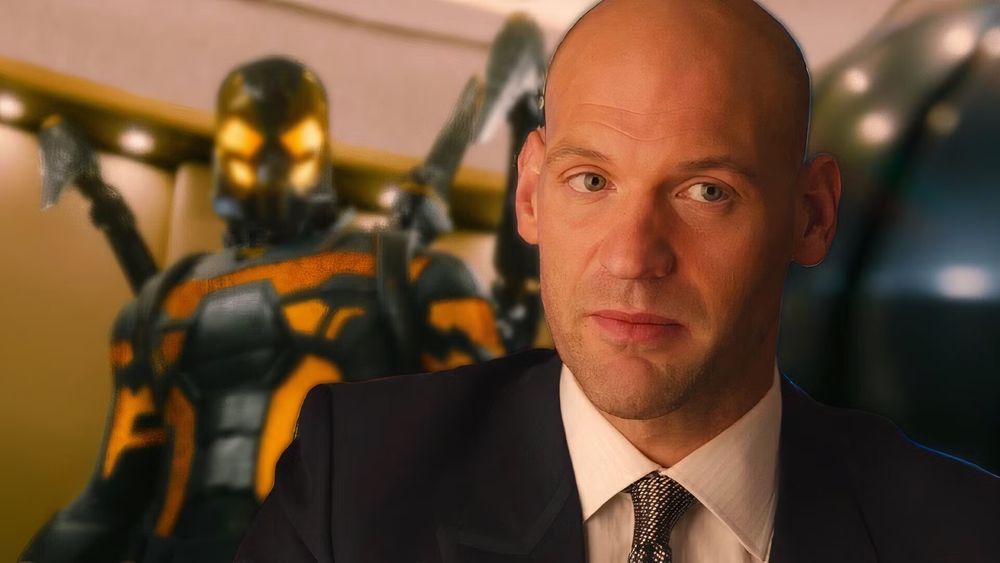 A bald Caucasian man in a business suit. Behind him looming out of focus is an armored suit with menacing appendages and a glowing mask. It's the Yellowjacket suit.