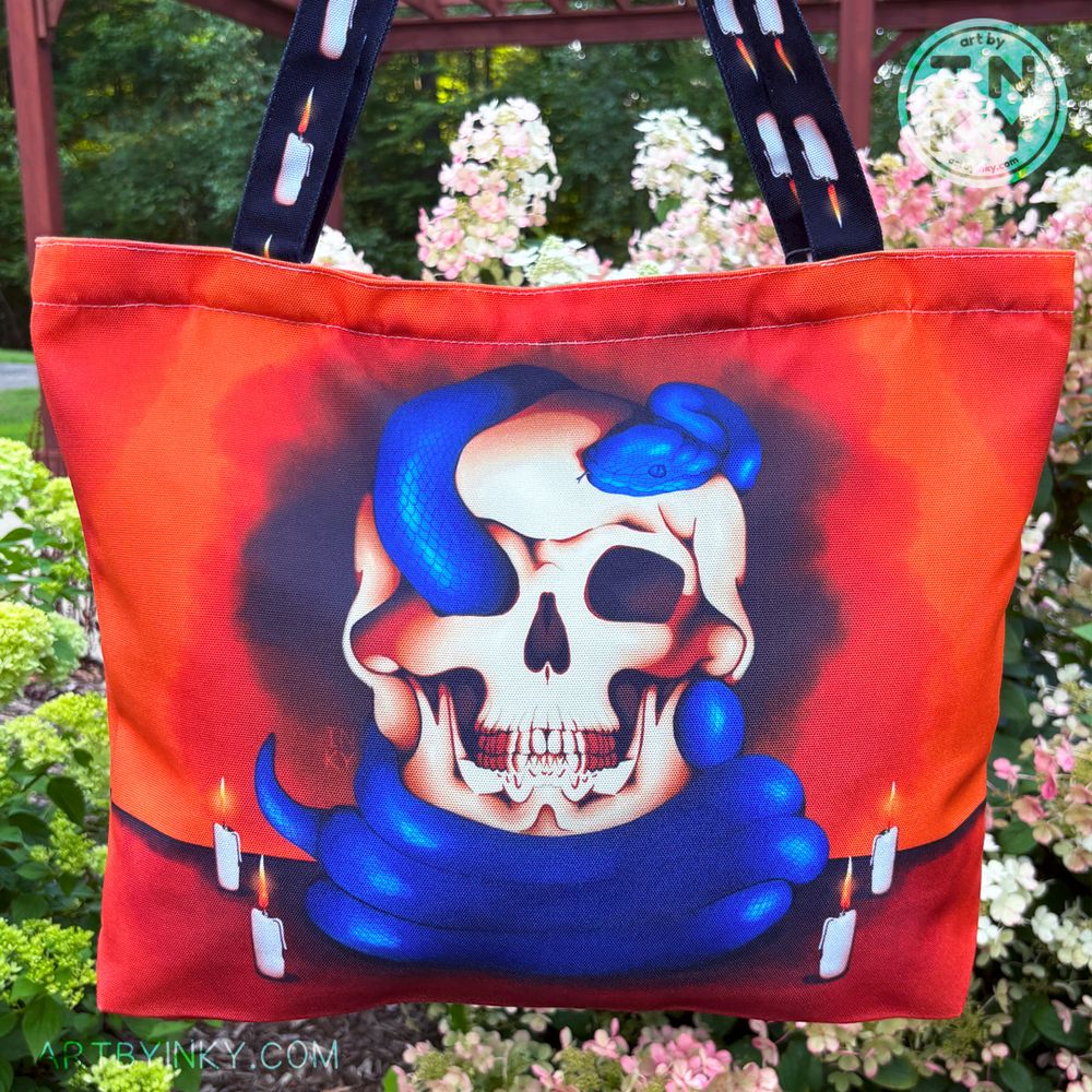 A blue snake and skull tote bag against a bush of flowers.