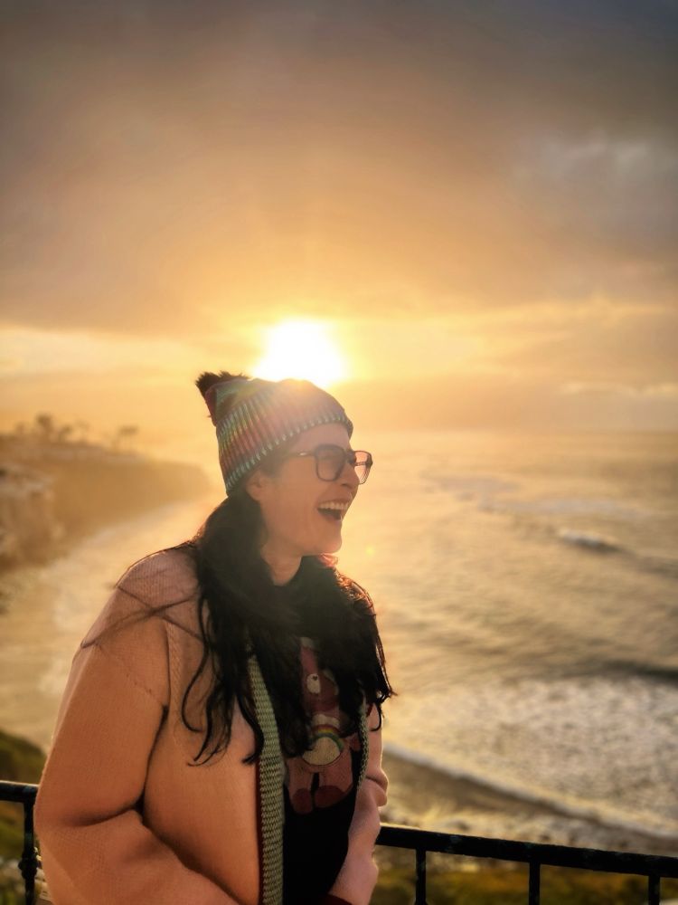 Sunrise over the Pacific Ocean and Christen Lien in a rainbow stocking hat, a Care Bear t-shirt with a big smile. 
