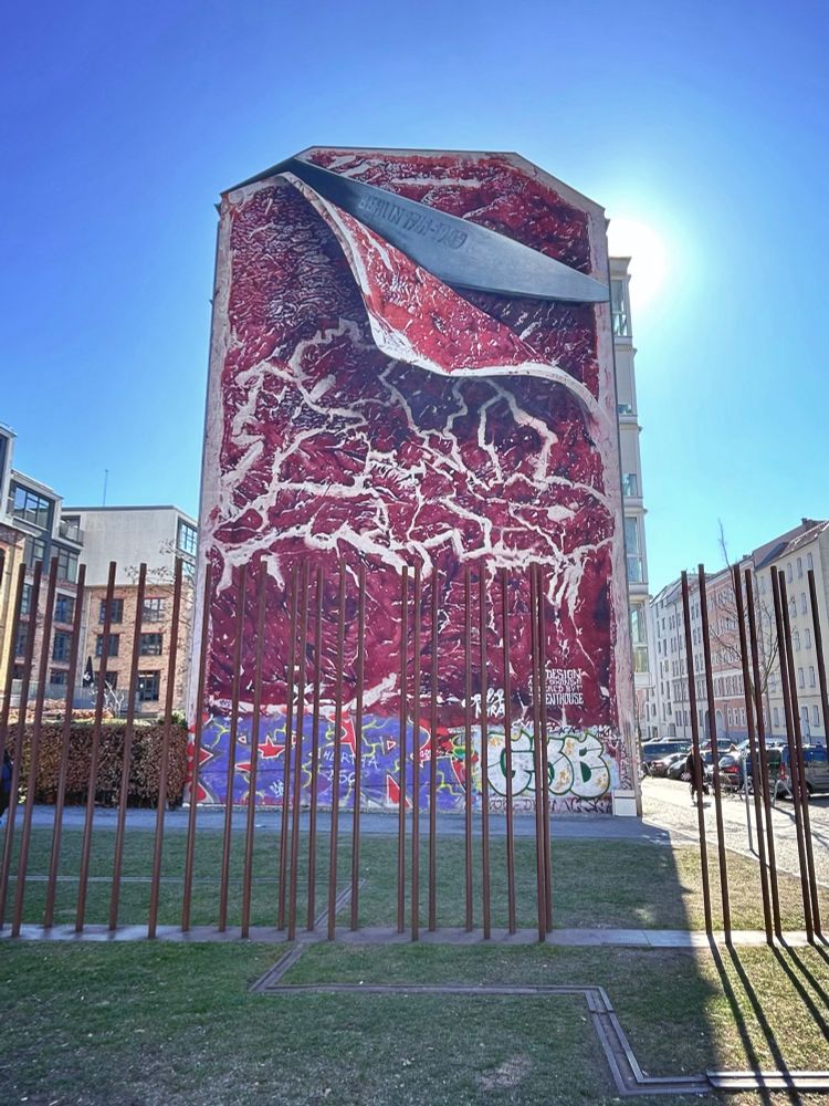 Mural at Bernauer Straße 11 in Berlin. The entire wall of the building is painted as raw meat. Atop a knife is cutting a piece of the meat. There is an inscription on the knife blade. It says: “Berlin 1961-1989”.