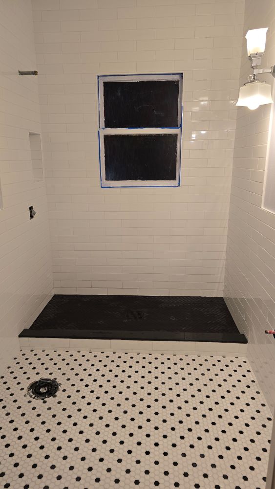  a fully tiled and grouted bathroom, white tile walls, black herringbone tile shower floor, black and white hex bathroom floor, no toilet or sink