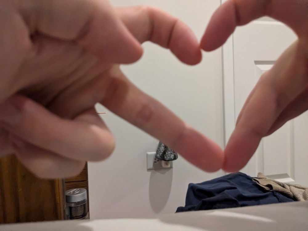 photo in a bedroom of my hands making a gen z heart somewhat badly