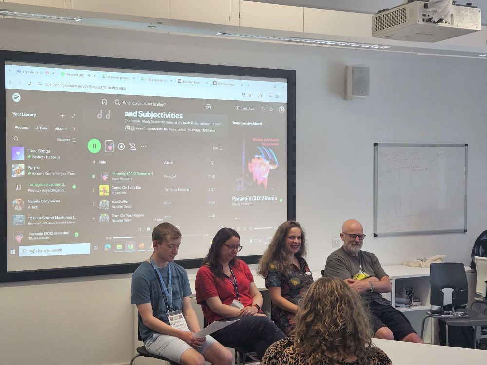 An image of the members of the Popular Music research cluster from BCMCR sitting in front of a projector screen showing a spotify playlist.