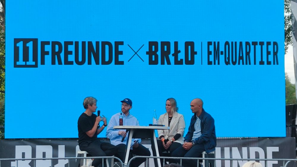 bühne des 11freunde-em-quartiers mit den sportchef*innen der frauen von union, viktoria und hertha jennifer zietz, catharina schimpf und sofian chahed sowie moderator louis richter. dahinter eine himmelblaue wand mit veranstaltungslogo