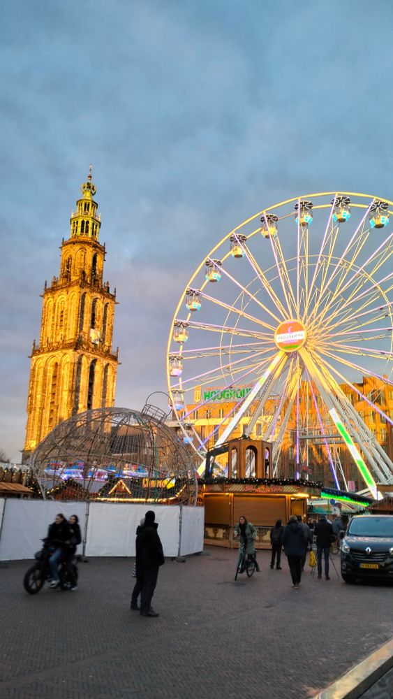 De Martinitoren verlicht door de laagstaande middagzon, met daarnaast een reuzenrad. 