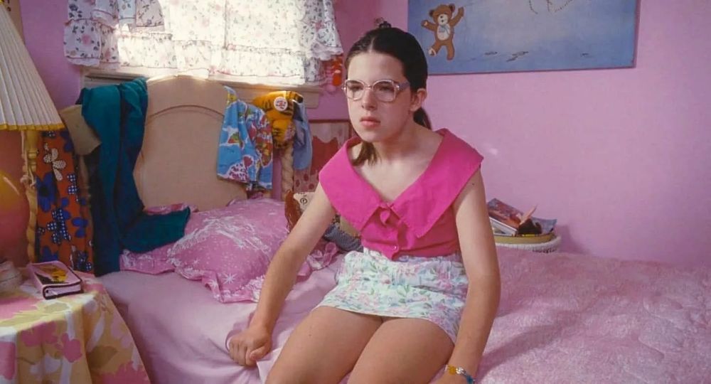 Heather Matarazzo as Dawn Wiener in WELCOME TO THE DOLLHOUSE (1995), looking uncomfortable dressed in a garish pink sleeveless top and floral print miniskirt that awkwardly frames her gangly adolescent frame--an ill-advised attempt to look cool and fit in with her judgmental classmates.