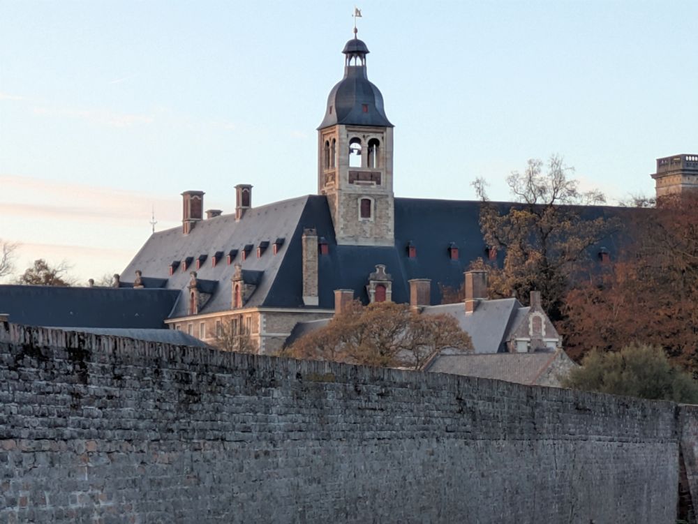Boven een oude stadsmuur steekt de toren van een seminarie uit. In het licht van de namiddag.