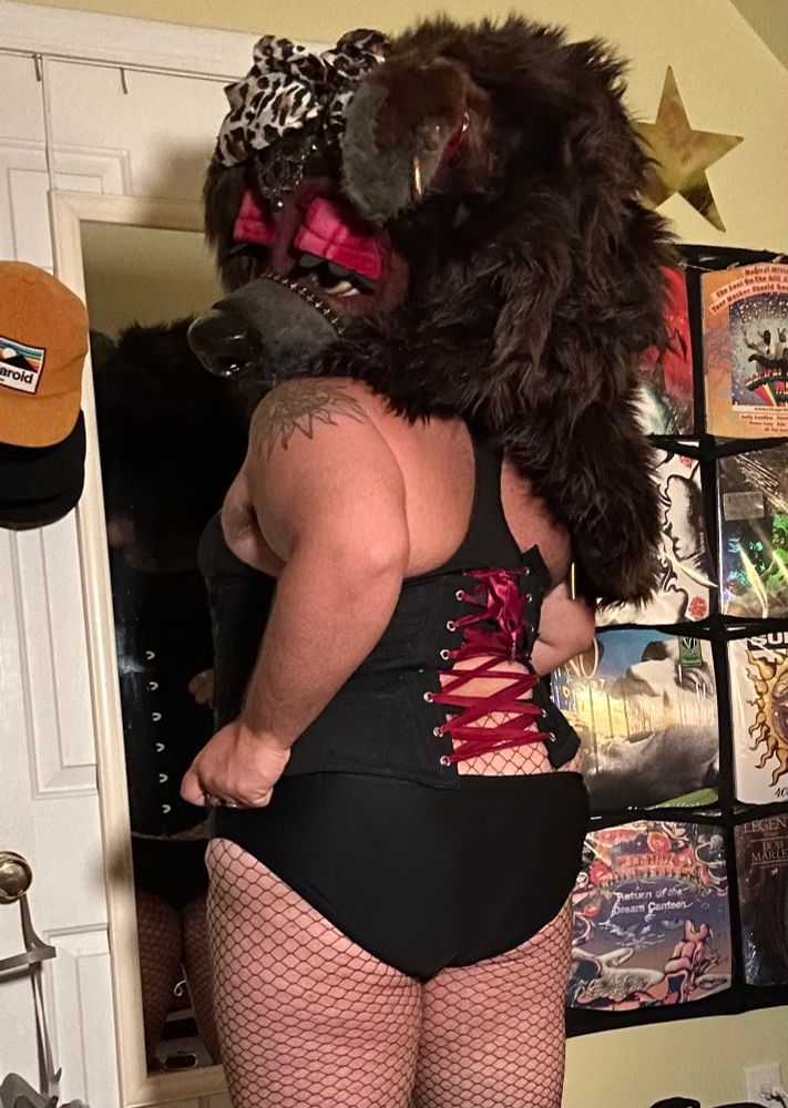 Bailey turned 3/4 backwards with both hands pulling down on her corset as she shows off her booty and the red lacing holding back her tummy