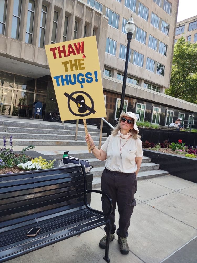 a woman in white floppy hat, t shirt and black pants holding sign that says thaw the thugs