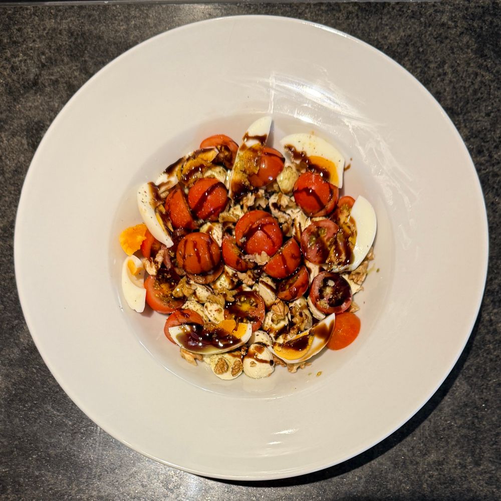 Weißer Teller mit Miniparadeisern, Minimozzarella, Nüssen, Eiern, Balsamicocreme