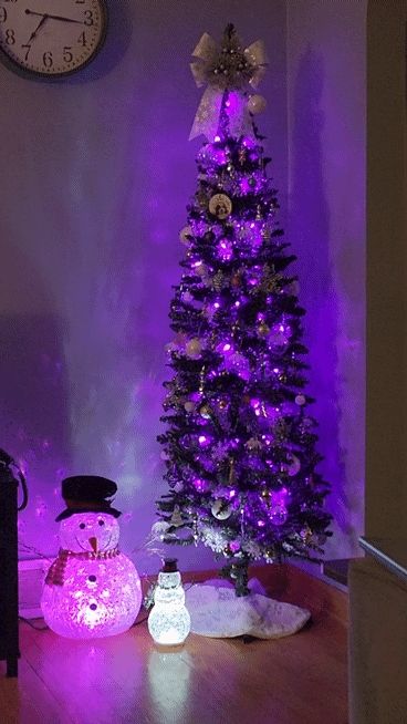A Christmas tree with purple lights and silver and white decorations,  with two sparkly lighted snowmen next to it