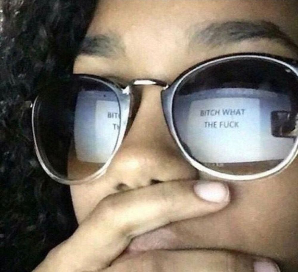 Girl with her hand over her mouth in shock,  "bitch what the fuck" visible in the reflection of her sunglasses