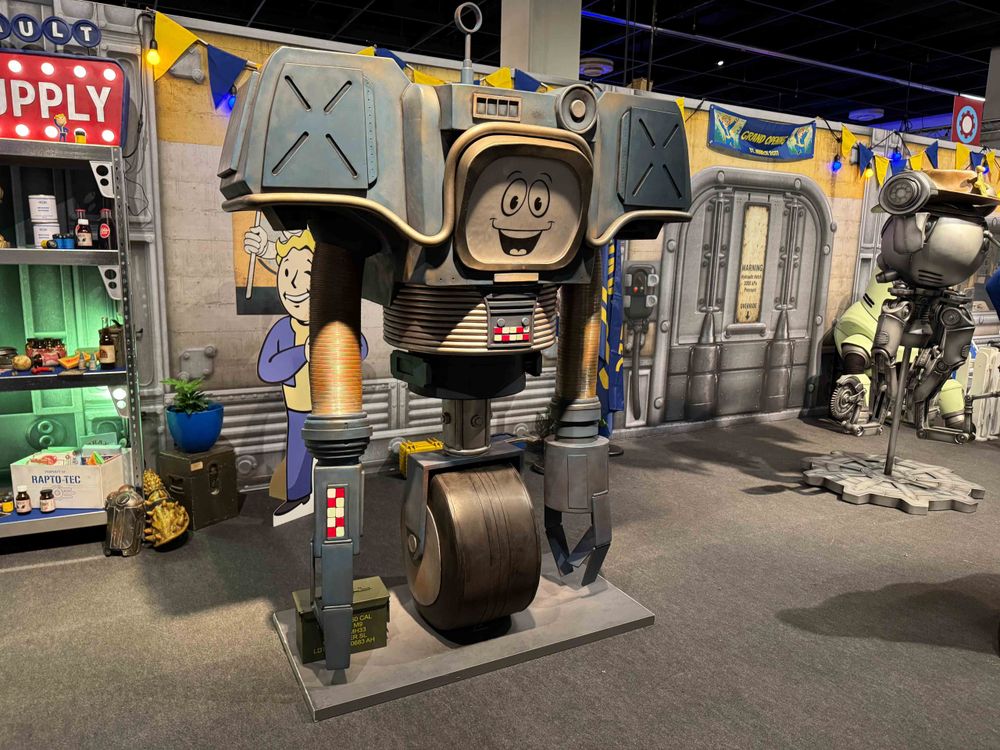 A photo of a Fallout-themed booth at Gamescom, including a vault background, Mr Handy, Yesman, and various small props