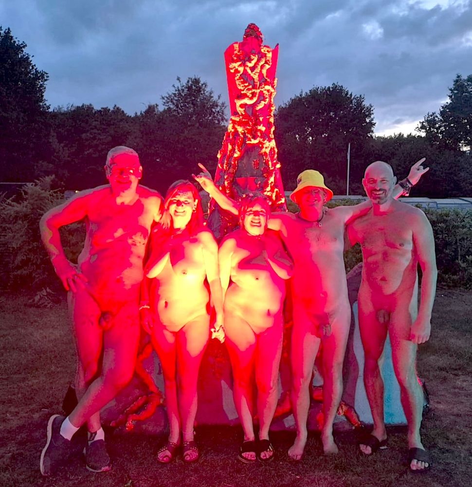 Five people, three men two women, stood in a line and smiling to the camera. They are in front of a model volcano and the picture is lit in bright red light.