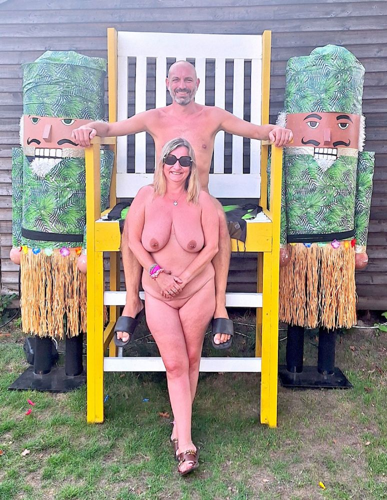 A man sat on an oversized chair, with a woman stood in front of the chair.