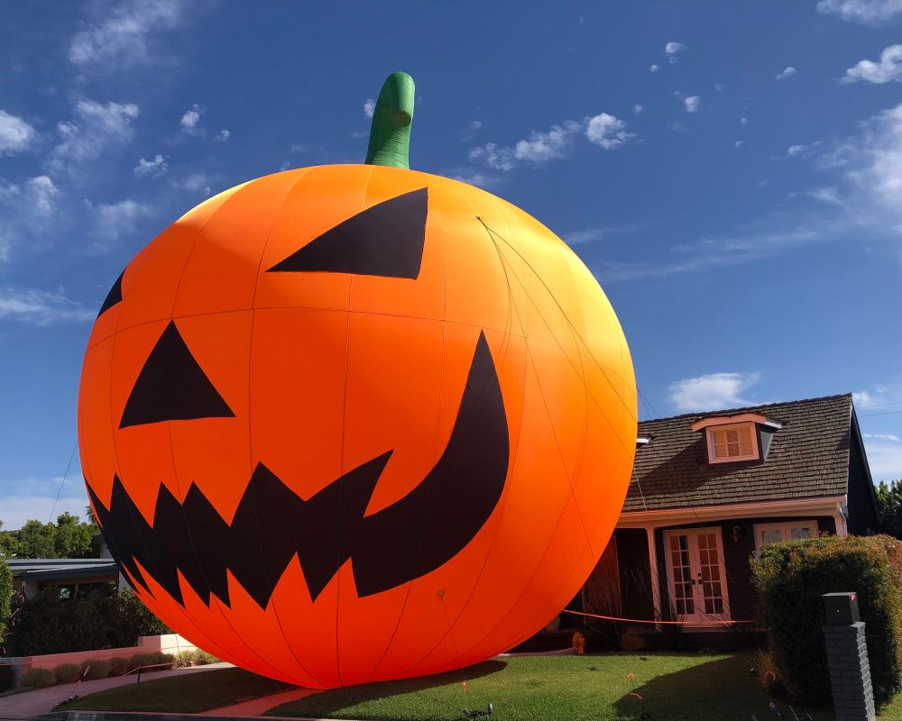 Inflatable lawn ornament designed as a jack-o-lantern, sitting upon a green lawn in front of a two story suburban home.
The lawn ornament is twice the height of the house and takes up the entire front yard.