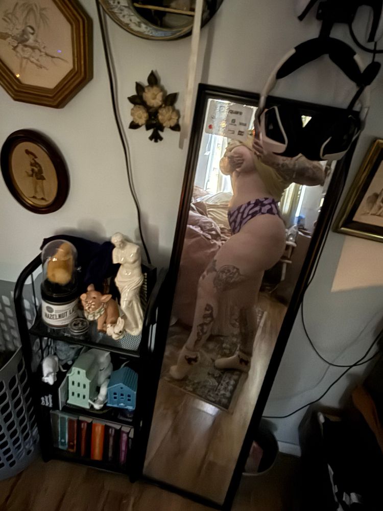 Mirror selfie of body in underwear. There’s a bookshelf with curiosities and books on it to the left of the long mirror. 