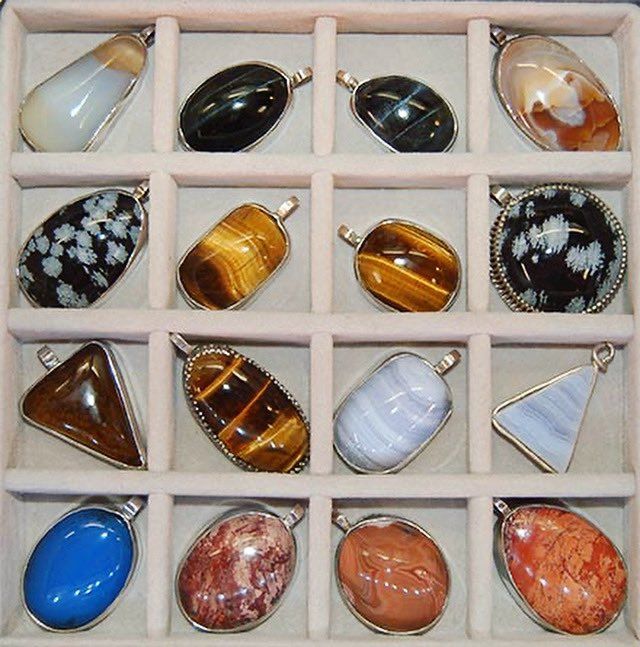 Cabochons of different minerals, mounted in silver to form pendants for necklaces. Each pendant is in its own compartment in a velvet lined jewellery box. 
