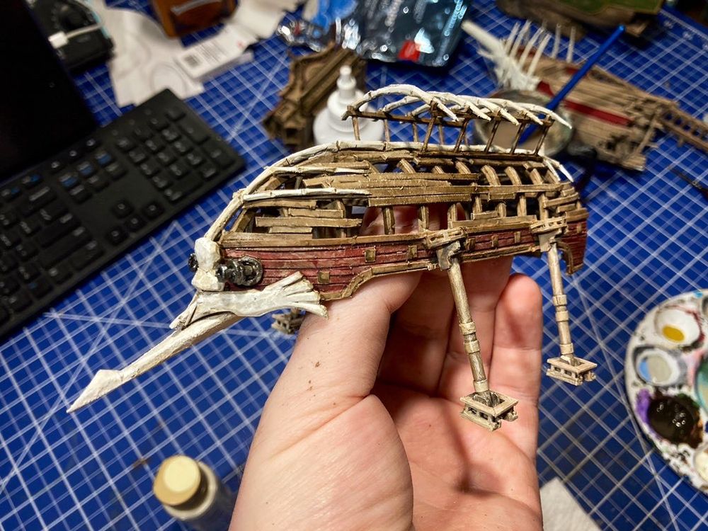 photo of a handmade model of the Tradeyard Canopy from Astera in Monster Hunter World. the canopy is an upside down ship hull with bone-like decoration and the model itself is built from paper.