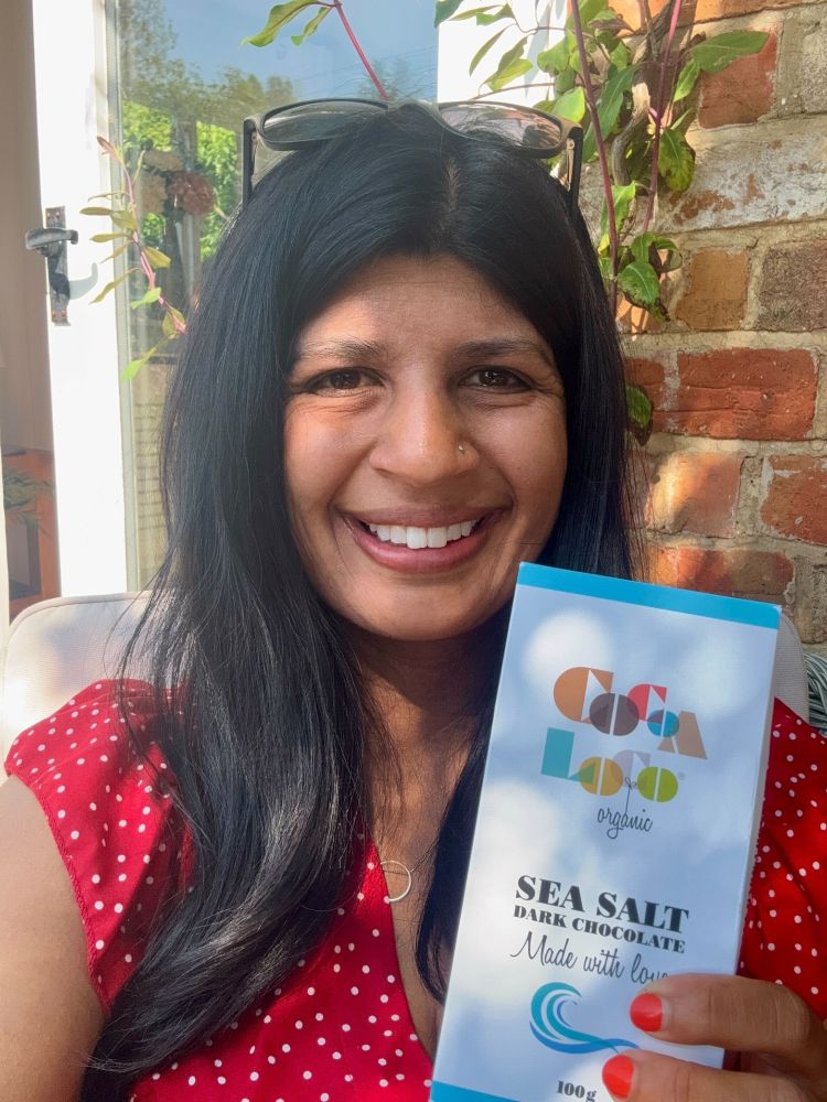 Jess takes a selfie with chocolate bar - she is sat in a sunny outside garden wearing a red dress.