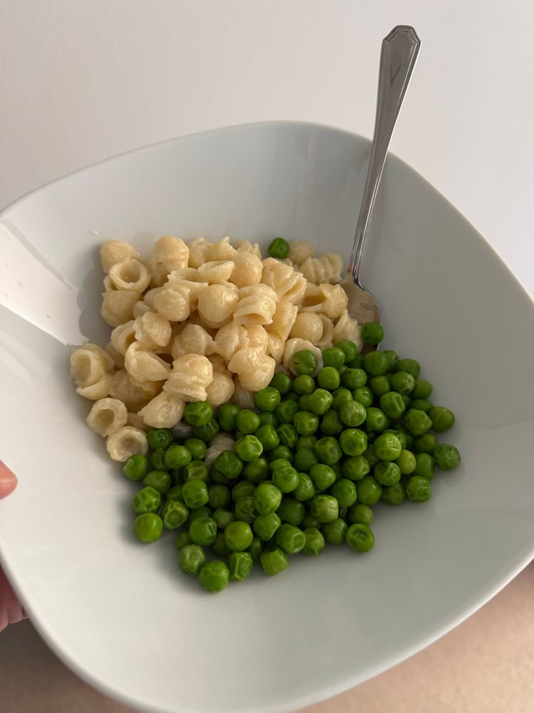 White square bowl with mac n cheese and green peas and a stainless steel spoon sticking out from the food