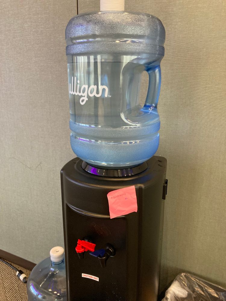 Photo of a water cooler with a post-it note attached saying “*beg for mercy”