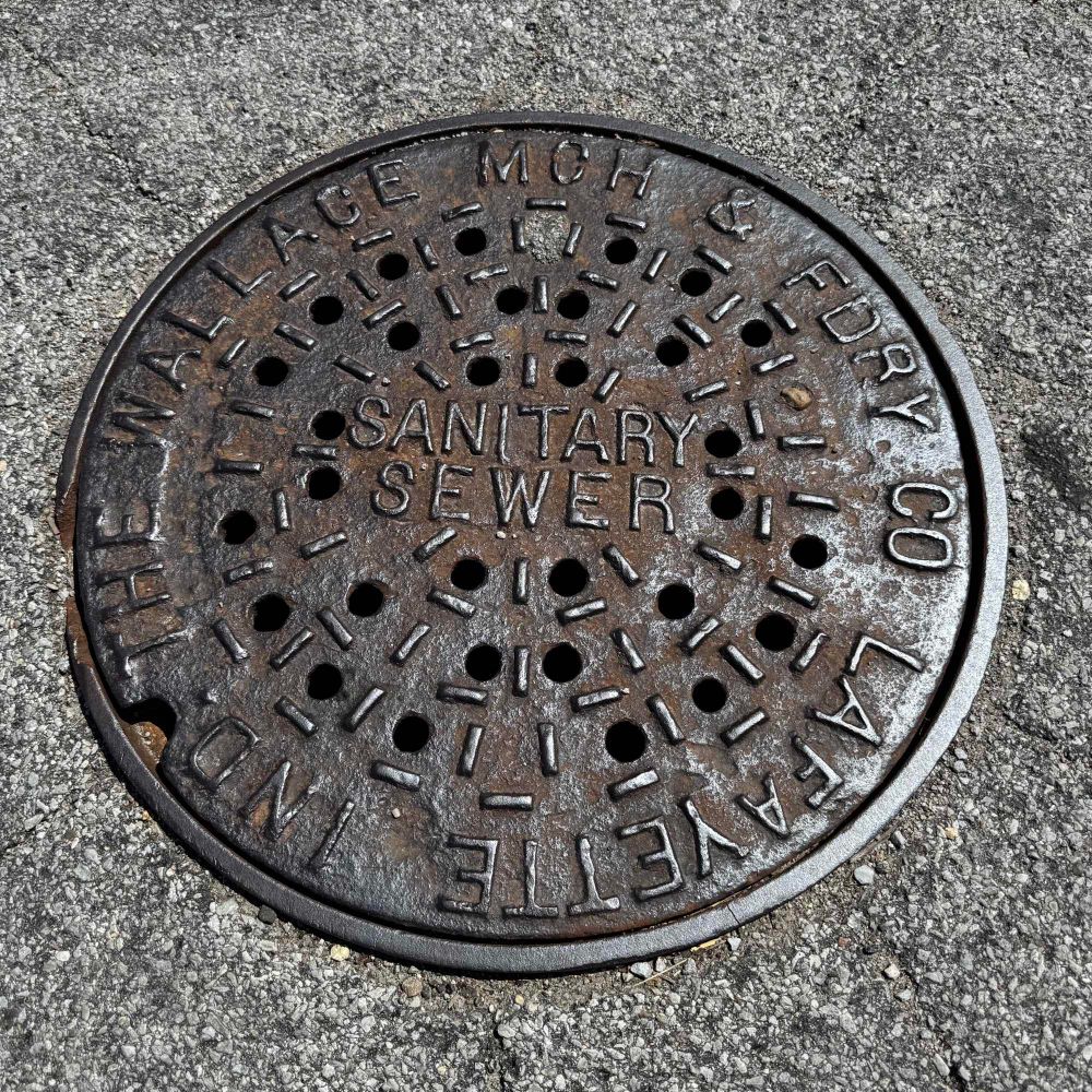 Well worn iron cover with a smattering of round holes and hash marks and the foundry, city and state names encircling it. 