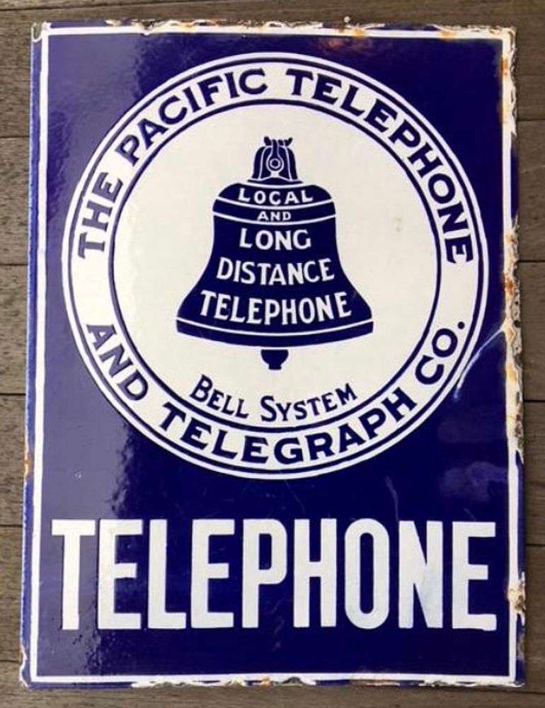 Vintage sign for The Pacific Telephone & Telegraph Co. has a bell-shaped logo at its center has these words on it, “Local and Long Distance Telephone” and below that, the words “Bell System.”
