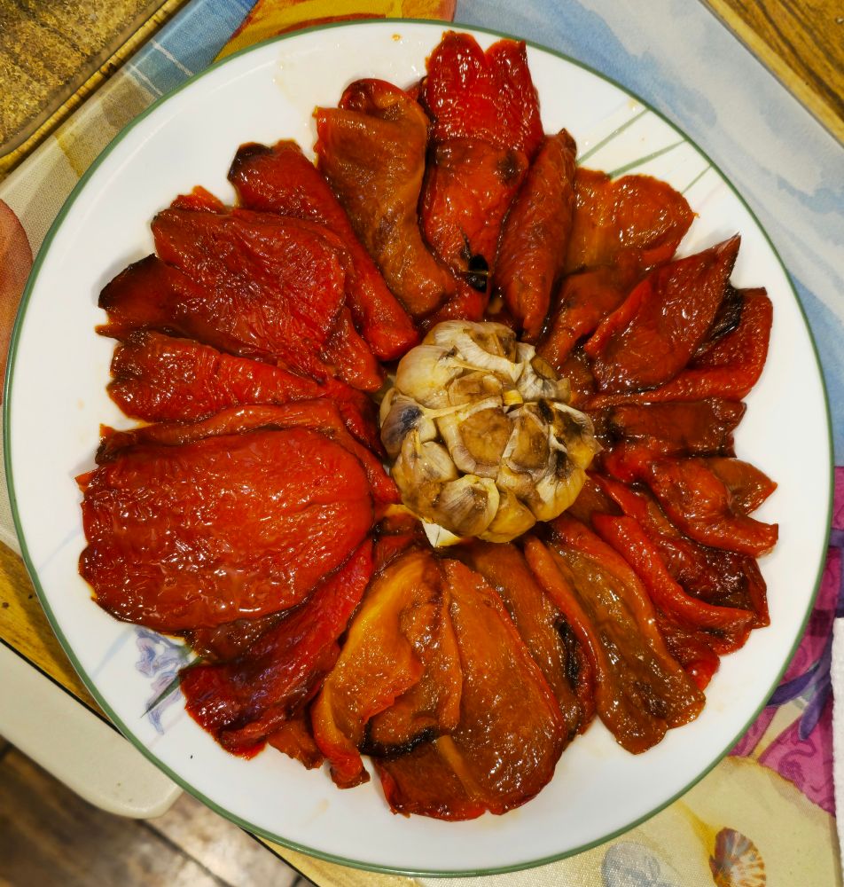Photo of roasted red peppers surrounding a bulb of roasted garlic. It looks like a flower.
