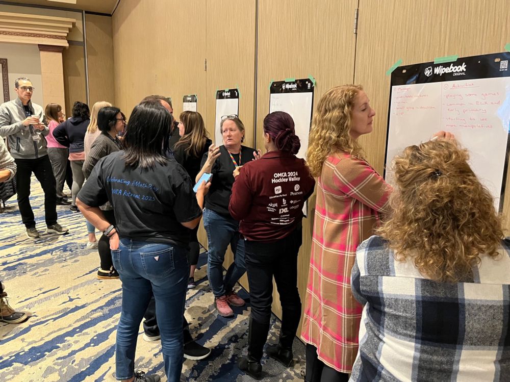 OMCA retreat participants standing in groups in front of whiteboards.