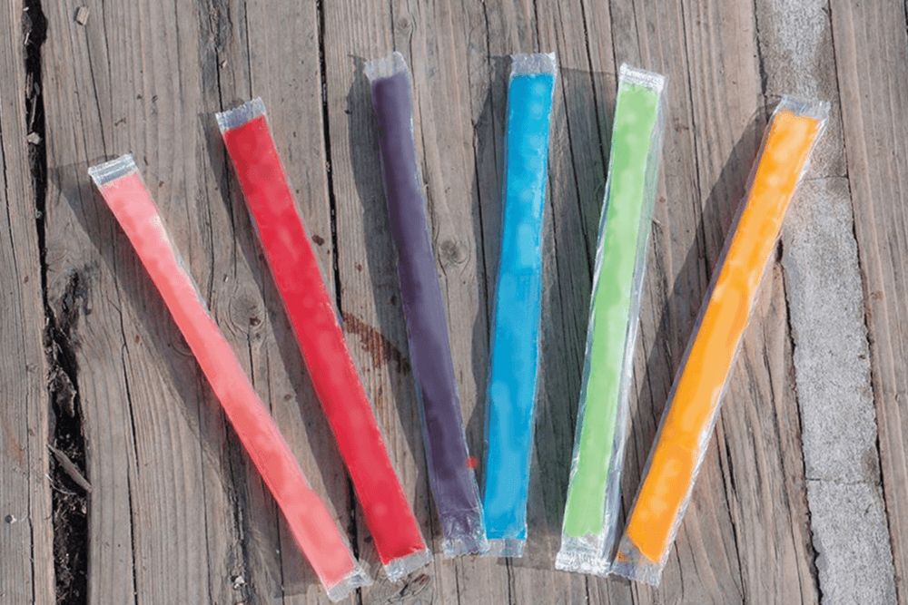 an array of multi-colored freeze pops laying outdoors on a wooden deck