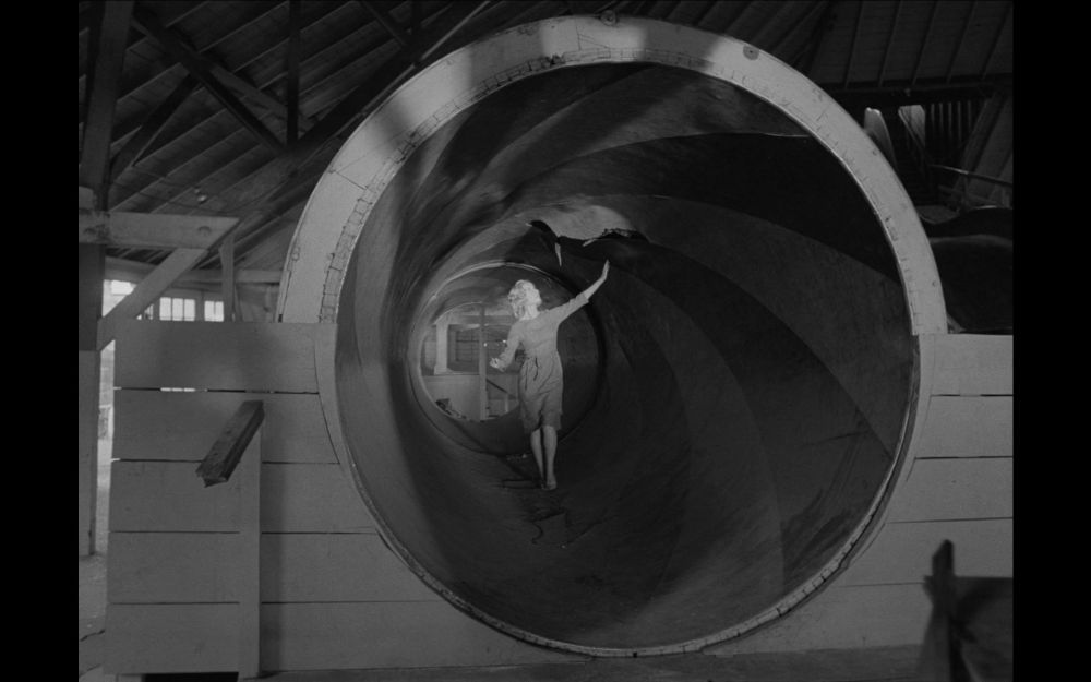 a woman in a cylindrical tunnel painted with stripes, creating the illusion she's very small