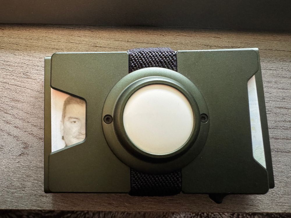 A metallic green wallet with an Apple AirTag built in. My drivers license is peeking out of the bottom showing only half of my face.