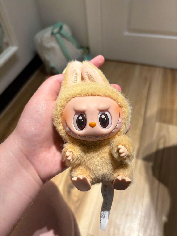 An image of a tan Labubu plush pendant, specifically Baba from the “Have a Seat” collection