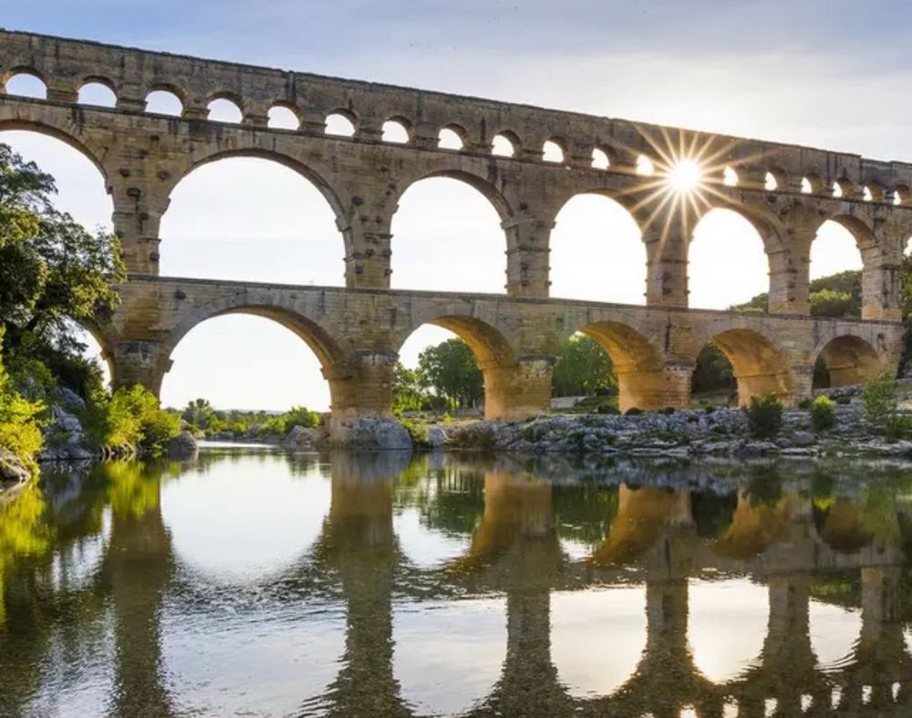 Die römische Brückenkonstruktion in Avignon eine aus 3 übereinander stehenden Bogenreihen bestehende Brücke - im Vordergrund spiegelt sich die Brücke im Fluss. Durch einen der oberen Bögen scheint die Sonne