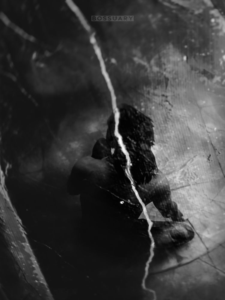 a black and white shot of lucanis from outside a crystalline enclosure. as he crouches inside the claustrophobic trap, the high angle reveals how vulnerable he seems in only a pair of briefs. the crystal facet through which we see him is cracked down the center, splitting the picture with a bright fissure.