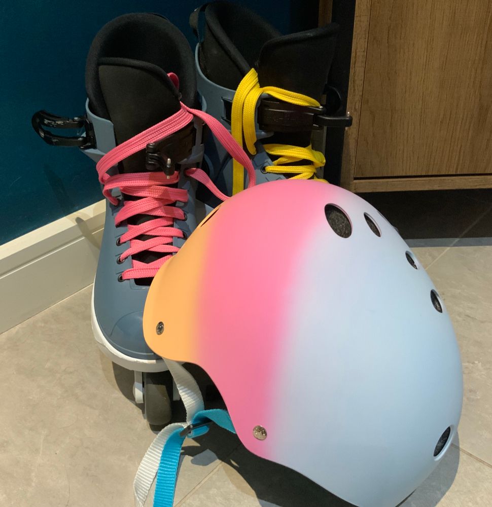 Roces Loco Blue M12 aggressive skates. One skate with pink laces and the other with yellow laces. Matching helmet, blue yellow and pink