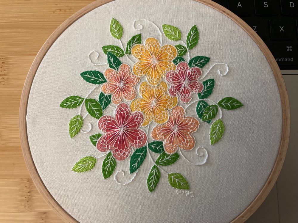 Lacy Flowers by Jessica Long: embroidered flowers in shades of pink, orange, and yellow with green leaves, with white stitches laid over them to create a lacy effect. 
