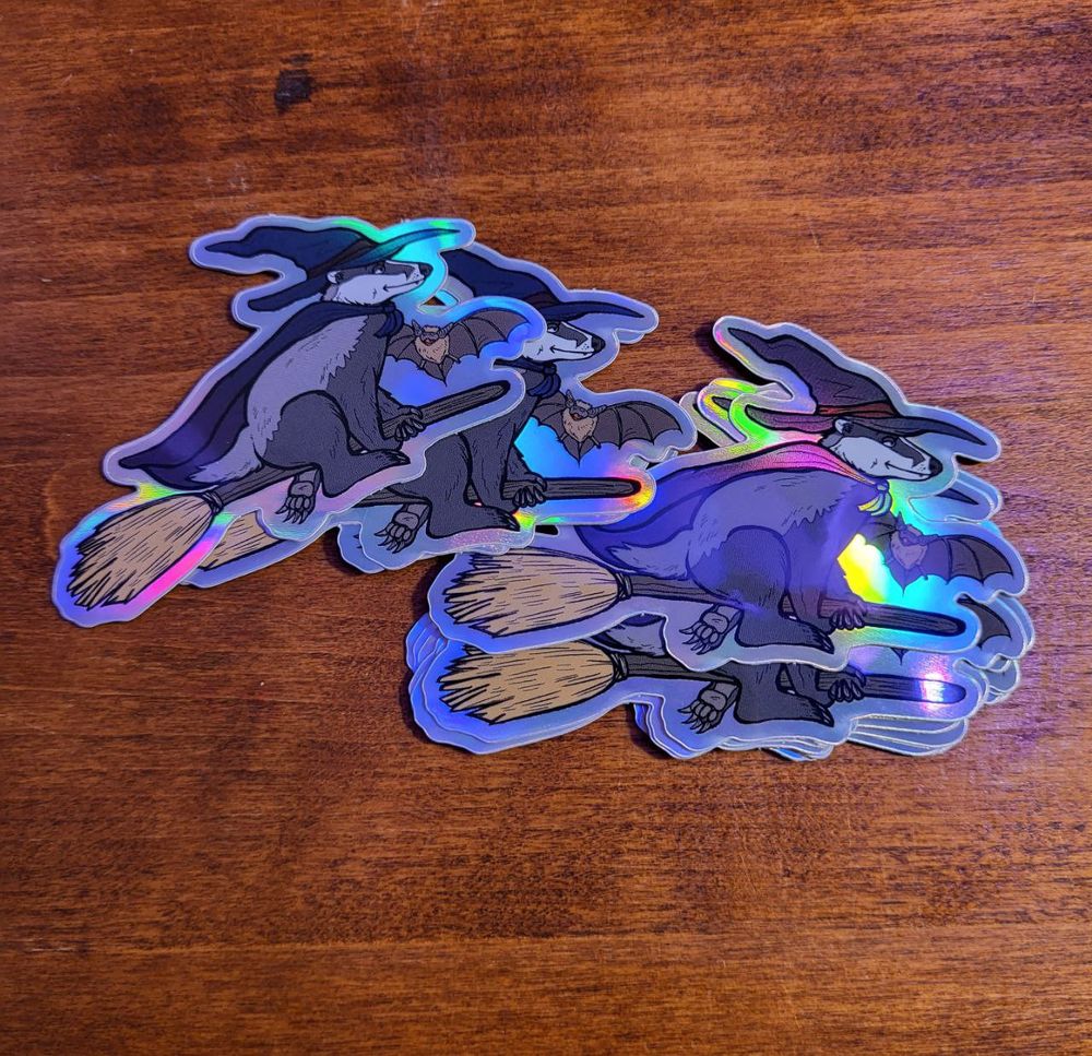 a pile of rainbow shimmer stickers with a design of a badger witch on a broomstick